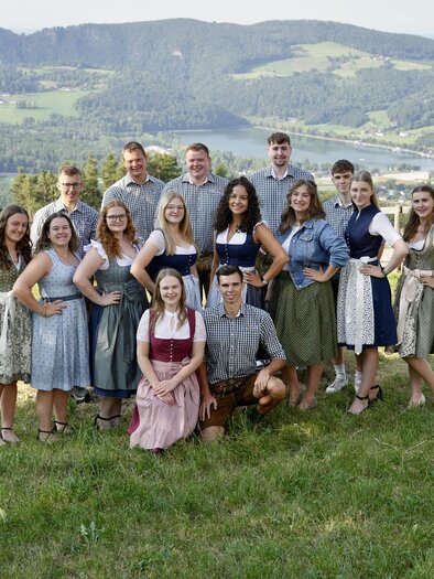 A group of people is standing in a meadow with a view of the mountains. They are wearing traditional clothing and smiling at the camera. | © Landjugend Stubenberg