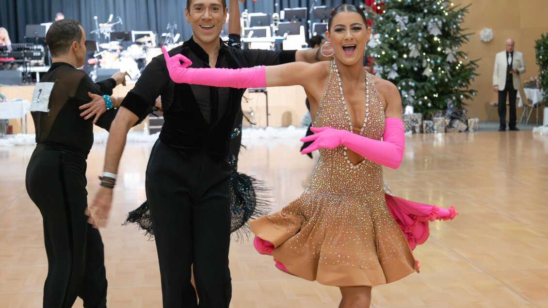 Ein Paar tanzt fröhlich auf der Tanzfläche. Im Hintergrund sind Weihnachtsdekoration und eine Band zu sehen. | © Dance Unity