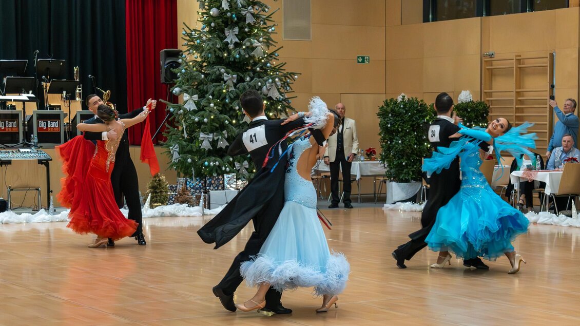 Tanzpaare in eleganter Kleidung zeigen ihre Fähigkeiten auf dem Parkett. Im Hintergrund steht ein festlich geschmückter Weihnachtsbaum. | © Dance Unity