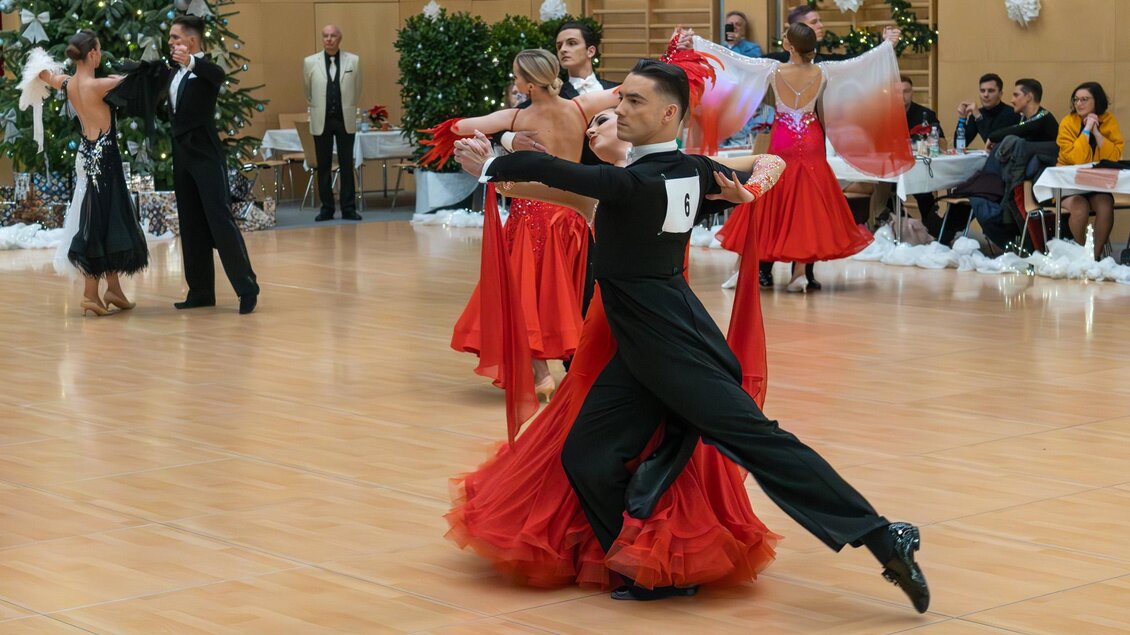Ein Tanzwettbewerb mit Paaren in eleganter Abendkleidung. Die Tänzer zeigen ihre Fähigkeiten auf der Tanzfläche, umgeben von festlicher Dekoration. | © Dance Unity