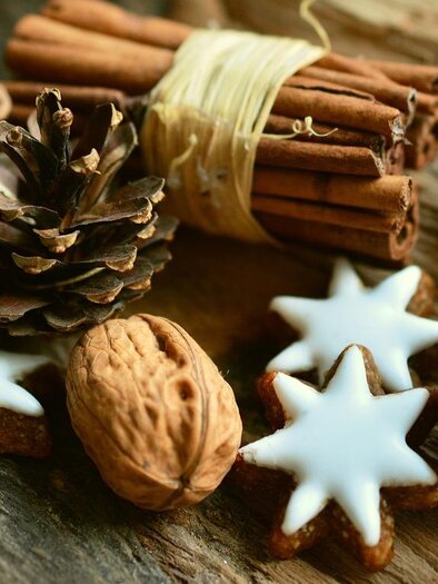A rustic wooden surface with cinnamon sticks, pine cones, nuts, and decorative star cookies. The combination of natural and baked elements creates a cozy, festive atmosphere. | © Pixabay.com
