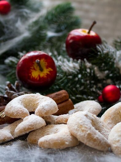A flat plate with delicious cookies, pine branches, and Christmas decorations. In the background, a glass with a hot beverage and red apples is visible. | © Pixabay.com