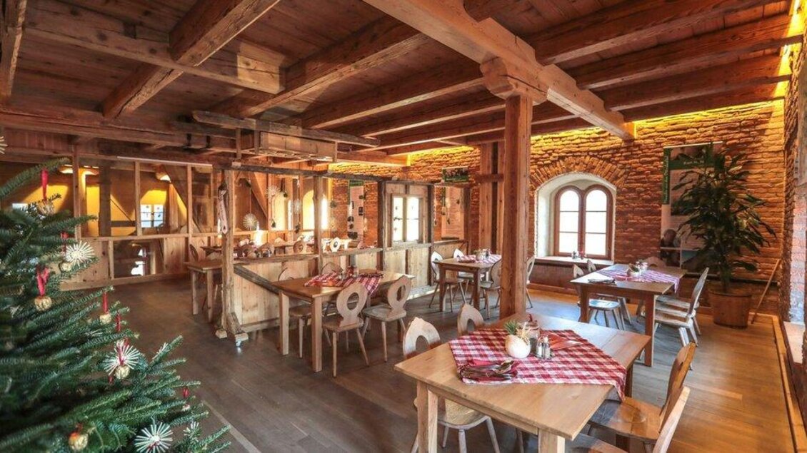Ein einladendes Restaurant mit Holzelementen und einem rustikalen Ambiente. Gemütliche Tische und eine festliche Weihnachtsdekoration schaffen eine warme Atmosphäre. | © © Foto De Monte