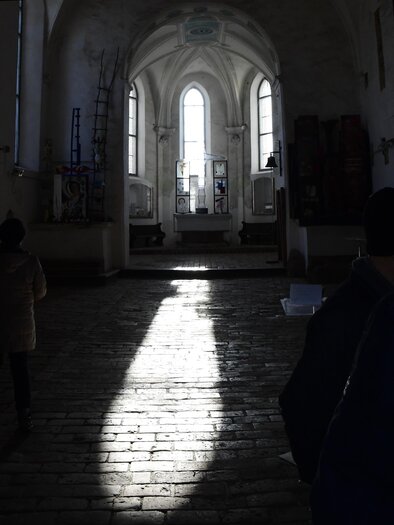 A dark, spacious interior with high windows through which soft light falls. The floor is made of wooden planks, and some people are visible in the room. | © Denise Ganster