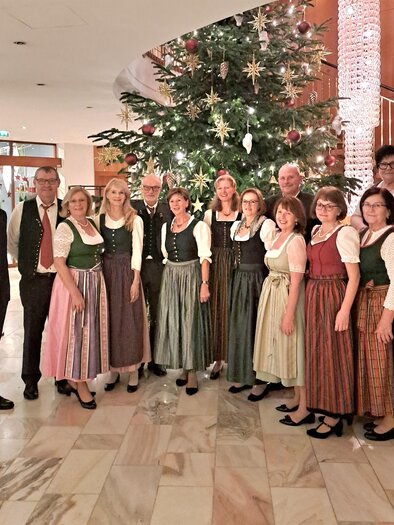 Eine Gruppe von Personen in traditioneller Tracht steht vor einem festlich geschmückten Weihnachtsbaum. Der Raum ist warm und einladend mit elegantem Ambiente. | © Glatz Herta