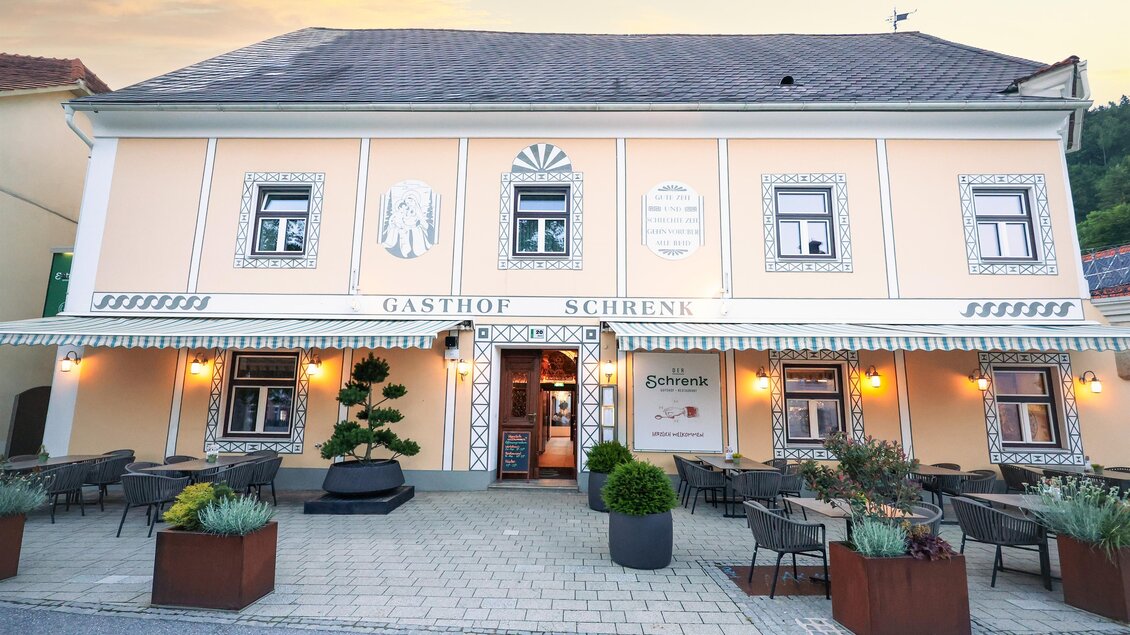 Ein traditionelles Gasthaus mit einer hellen Fassade und Fenstern. Vor dem Eingang befinden sich Tische und Pflanzen. | © Der Schrenk