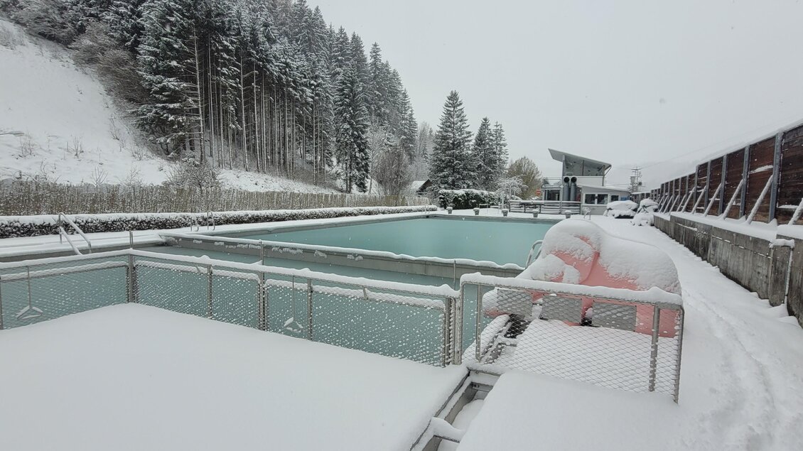 Ein ruhiger Außenbereich mit einem Pool, der von Schnee umgeben ist. Im Hintergrund sind verschneite Bäume und eine stilvolle Architektur zu sehen. | © Tim Fuchsberger 