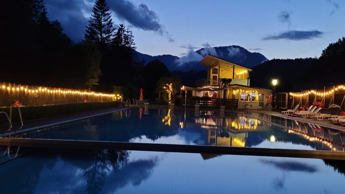 Ein schöner Pool bei Dämmerung, umgeben von Bäumen und beleuchtet von Lichtern. Im Hintergrund ist ein kleines Gebäude sichtbar. | © Tim Fuchsberger 