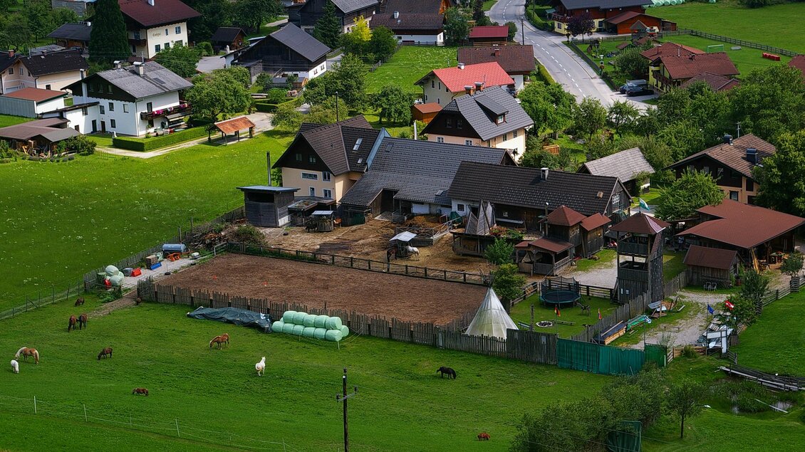Eine ländliche Umgebung mit mehreren Häusern und einem Hof. Das Gras ist grün und es sind einige Tiere auf der Weide. | © Abenteuerhof Schiefer