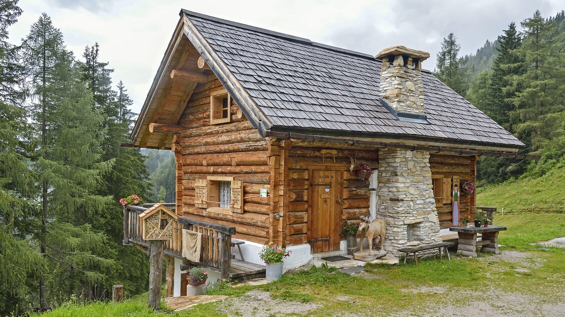Eine gemütliche Blockhütte umgeben von grünen Wäldern und Bergen. Der Kamin und die Holzverkleidung verleihen ihr einen rustikalen Charme. | © Herfried Marek