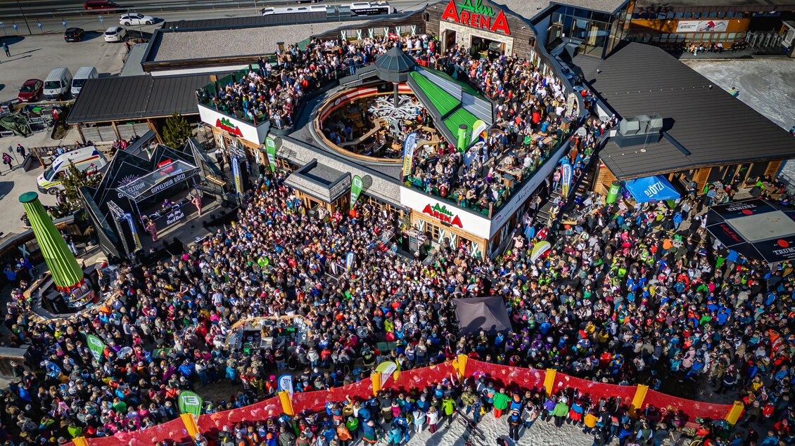 Große Menschenmenge feiert vor der „AlmArena“ bei einem Open-Air-Konzert, Bühne und DJ-Setup, bunte Fahnen und Banner schmücken das Gelände. | © AlmArenA