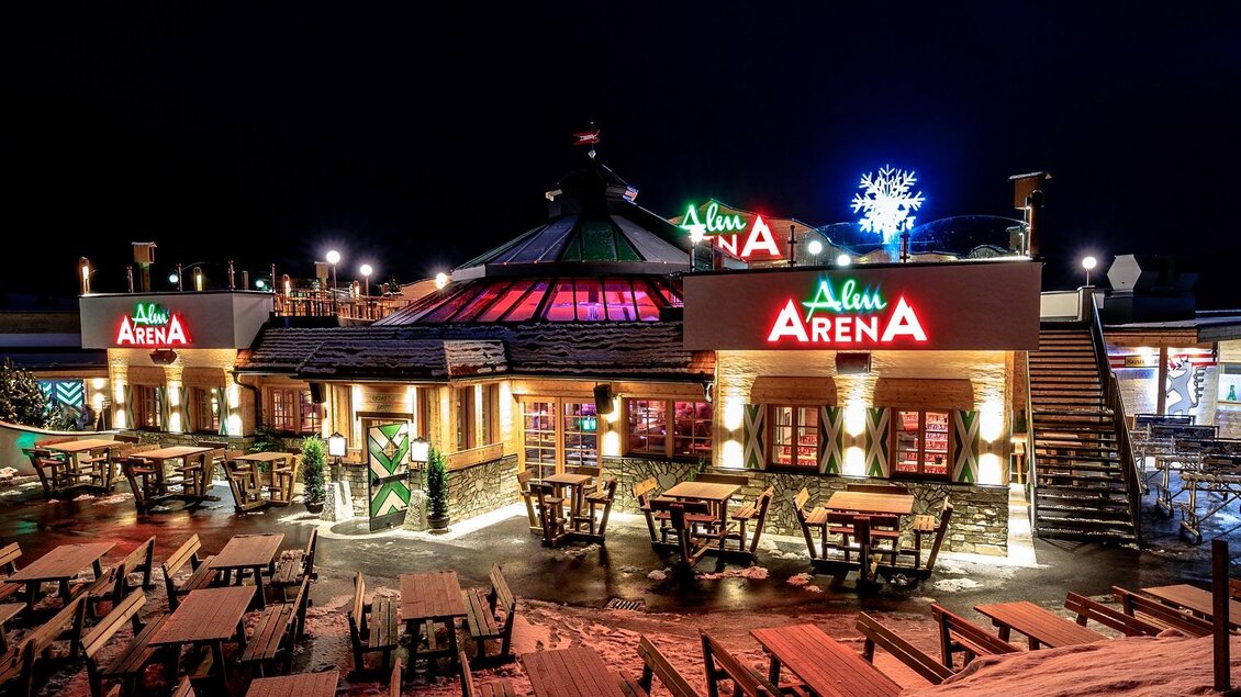 Ein modernes Restaurant mit beleuchtetem Dach, das in der Nacht gut sichtbar ist. Es gibt viele Tische im Freien und eine festliche Atmosphäre. | © Hauser Kaibling