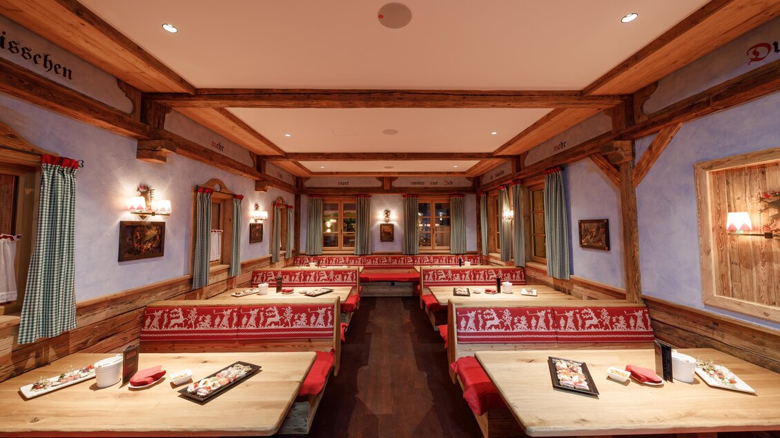 Ein gemütliches Restaurant mit Holzmöbeln und roten Sitzbänken. Die Wände sind in sanften Farben gestaltet, mit dekorativen Elementen. | © AlmArenA