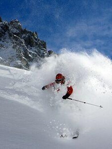 A skier glides vigorously through fresh, powdery snow. In the background, impressive rocks and a blue sky can be seen. | © Alpinschule Dachsteinguides