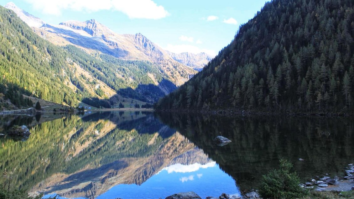 Ein ruhiger See, umgeben von hohen Bergen und dichten Wäldern. Die glatte Wasseroberfläche spiegelt die Landschaft wider. | © Livia Lassacher