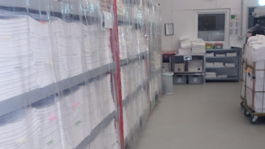 Ein Raum mit Regalen, die sauber gefaltete Handtücher lagern. Im Hintergrund sind weitere Ablageflächen und ein Fenster sichtbar. | © Amadé Textilservice GmbH