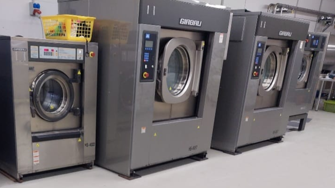 Moderne Waschmaschinen in einer gewerblichen Wäscherei. Die Maschinen sind groß, silber und stehen nebeneinander in einem sauberen Raum. | © Amadé Textilservice GmbH