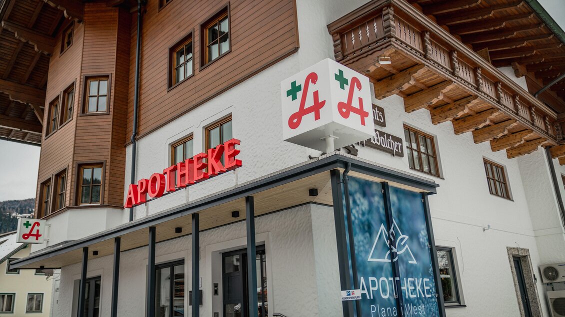Eine Apotheke mit einem modernen Gebäude im alpinen Stil. Große Schilder deuten auf die Dienstleistungen hin. | © Apotheke Planai West KG