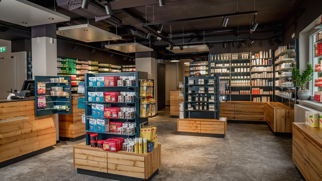 Ein modern gestalteter Laden mit Holzregalen und einer klaren, strukturierten Anordnung von Produkten. Die Wände sind mit verschiedenen Lebensmitteln und Artikeln zum Verkauf dekoriert. | © Apotheke Planai West KG