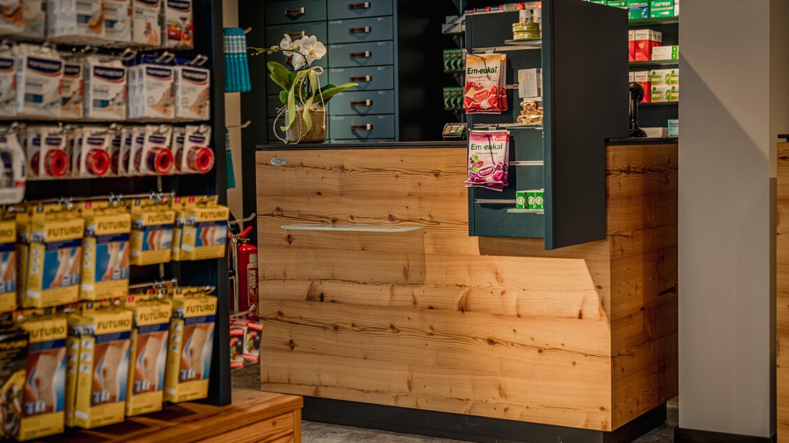 Ein modernes Ladengeschäft mit einer Holztheke und bunten Regalen. Auf der linken Seite sind verschiedene Produkte ordentlich ausgestellt. | © Apotheke Planai West KG