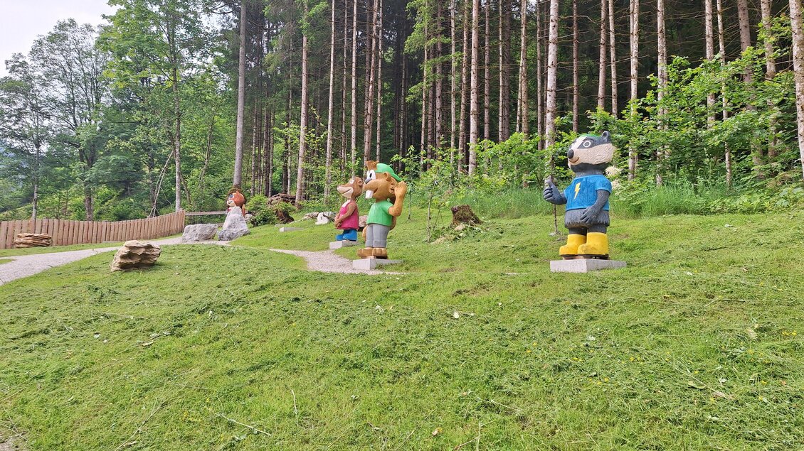 Eine Gruppe bunter Figuren steht auf einer Wiese im Wald. Im Hintergrund sind hohe Bäume und eine gepflegte Umgebung zu sehen. | © Nadine Schrempf