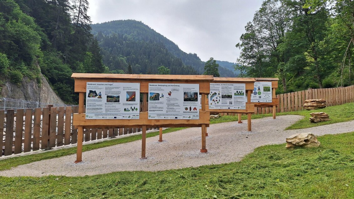 Ein Informationsbereich mit Holztafeln in der Natur. Im Hintergrund sind Bäume und Hügel zu sehen. | © Nadine Schrempf