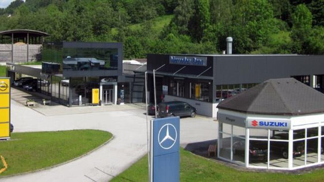 Ein Autohaus mit verschiedenen Marken wie Mercedes und Suzuki. Im Hintergrund sind grüne Hügel und ein blauer Himmel zu sehen. | © Auto Pfleger