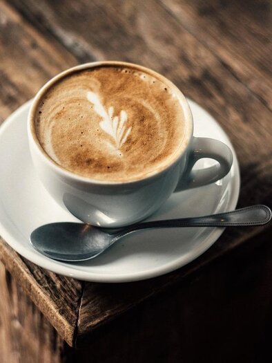 Eine Tasse Kaffee mit schöner Latte-Art auf einem weißen Unterteller. Der Hintergrund besteht aus einer rustikalen Holzoberfläche. | © Symbolfoto Pixabay