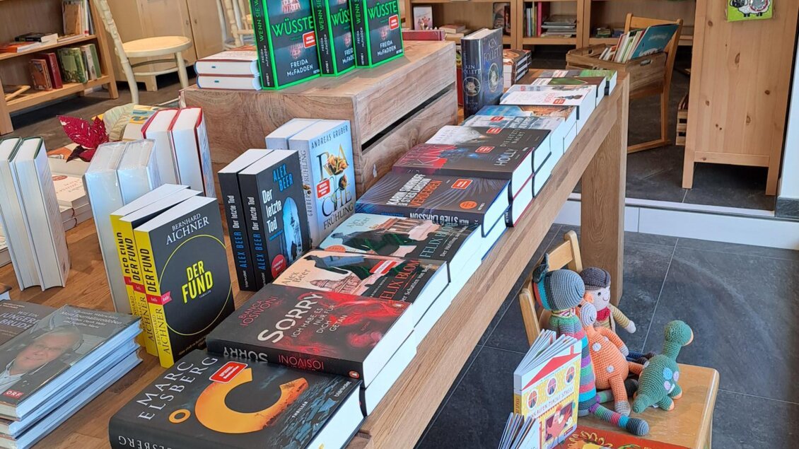 Ein gemütlicher Buchladen mit Regalen voller Bücher. Auf einem Holztisch sind verschiedene Bücher und Kinderspiele ausgestellt. | © Bücher Geschenke und mehr