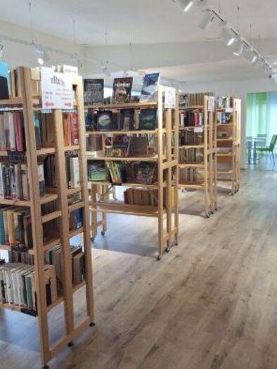 A modern library with wooden shelves full of books. In the background, tables and chairs are visible, creating an inviting atmosphere. | © Bücherei Schladming