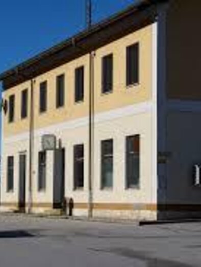 A modern, yellow building with several windows and a clear blue sky. In the foreground, a parking lot with a car is visible. | © Ennstal Wiki