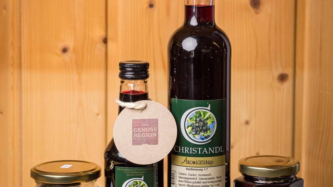 Verschiedene Flaschen und Gläser mit Konfitüren und Likören stehen auf einem Holztisch. Die Produkte sind elegant etikettiert und stammen aus der Region. | © Bauernladen Gröbming