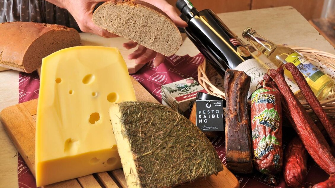 Ein rustikaler Tisch mit verschiedenen Käsesorten, Brot und Wurst. Dazu gehören auch Olivenöl und andere Delikatessen. | © Marianne Ritzinger 