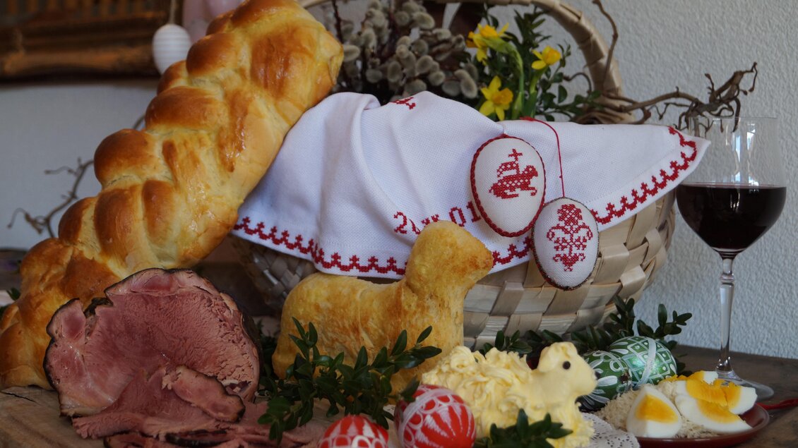 Ein festlicher Tisch mit einem geflochtenen Brot, einem dekorativen Lamm aus Teig und Ostereiern. Neben einem Glas Wein und einer schönen Serviette sieht man auch zartes Fleisch und seine Beilagen. | © Marianne Ritzinger 