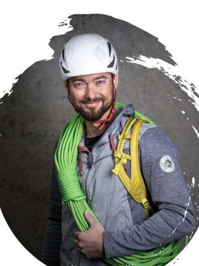 A man with a helmet stands with a green climbing rope over his shoulder. He is smiling and wearing a sporty jacket. | © Christoph Schwaiger