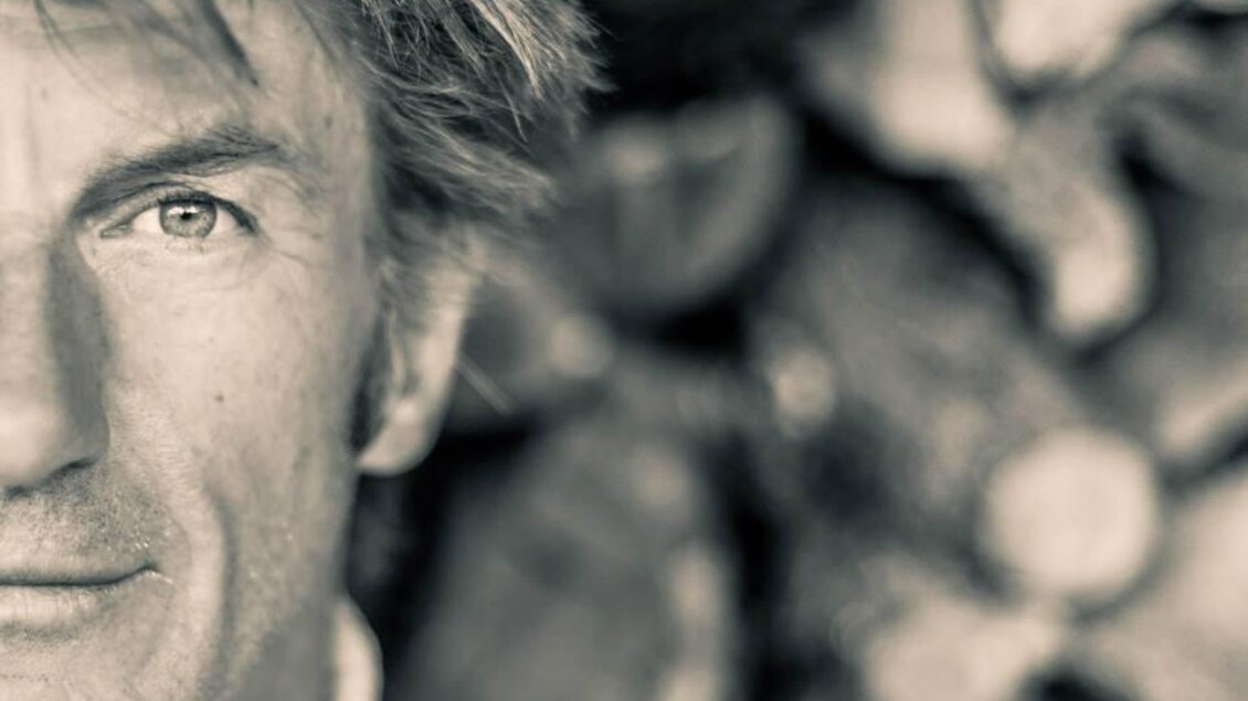 Ein Porträt eines Mannes mit unordentlichem Haar und einem nachdenklichen Blick. Der Hintergrund besteht aus Holzscheiten, die eine rustikale Atmosphäre schaffen. | © Monte-Krah5