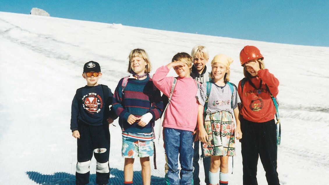 Eine Gruppe von sechs Kindern steht auf einem schneebedeckten Hang. Sie tragen bunte Kleidung und lachen in die Kamera. | © Monte-Krah