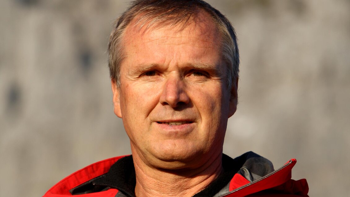 Ein Mann in einer roten Jacke steht vor einer felsigen Landschaft. Der Himmel ist klar und blau. | © Heri Eisl