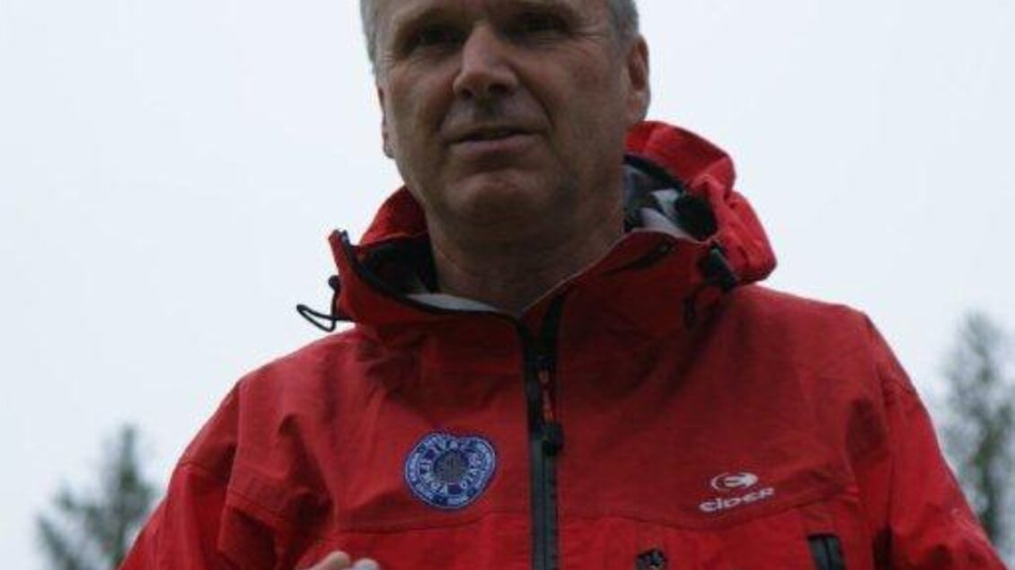 Ein Mann in einer roten Jacke hält ein Seil in der Hand. Im Hintergrund sind Bäume und ein grauer Himmel zu sehen. | © Heri Eisl