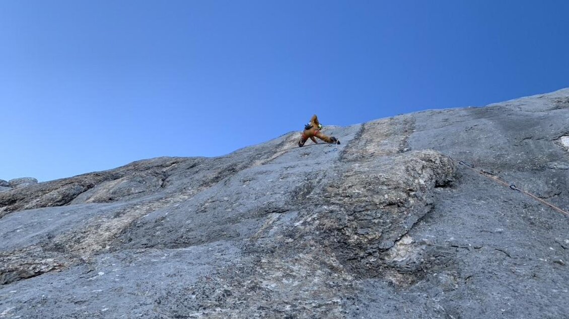 Ein Kletterer, der eine steile Felswand erklimmt, vor einem klaren blauen Himmel. Der Felsen ist grau und rau, was die Herausforderung des Kletterns betont. | © Peter Perhab