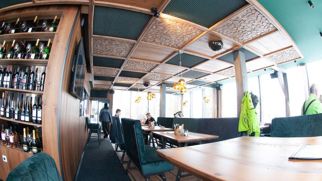 Ein modernes Restaurant mit Holzpaneelen und stilvollem Design. Es gibt mehrere Tische und eine beleuchtete Bar im Hintergrund. | © Knappl's Bergschlössl