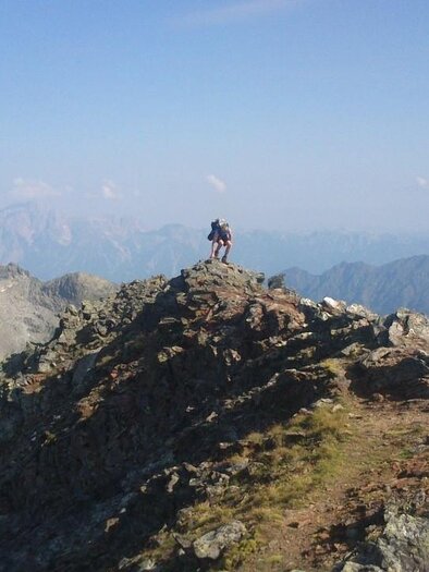 Ein Wanderer steht auf einem schmalen Bergrücken mit beeindruckender Aussicht auf Bergketten. Der Himmel ist klar und die Landschaft ist von grünen und grauen Tönen geprägt. | © Martin Huber