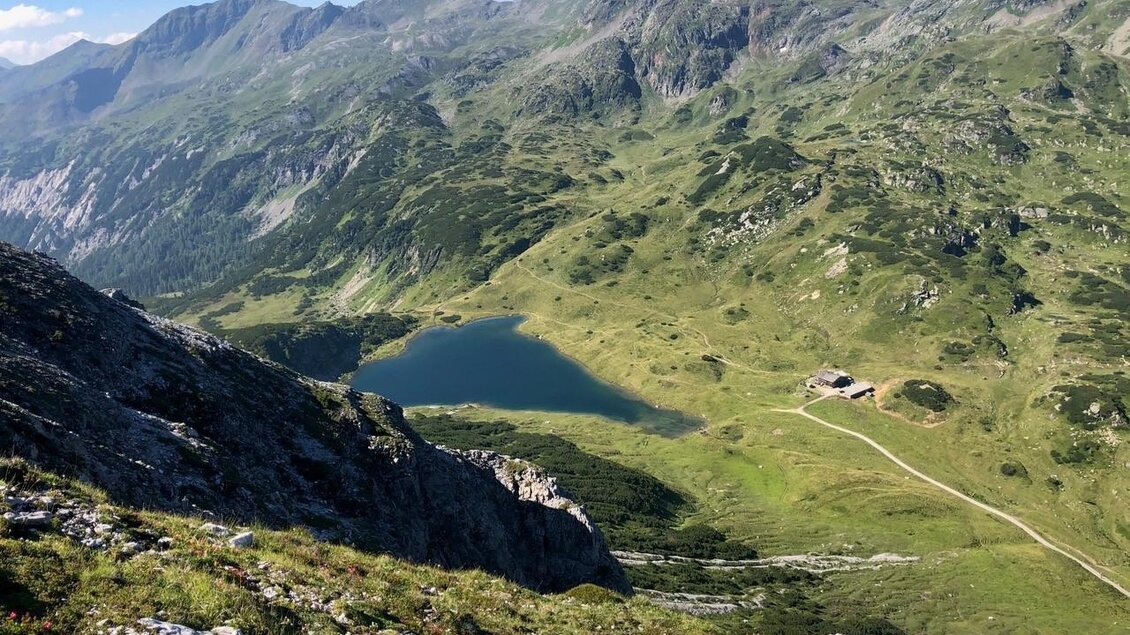 Eine malerische Berglandschaft mit grünen Wiesen und einem klaren See. Im Hintergrund sind majestätische Berge zu sehen. | © Martin Huber