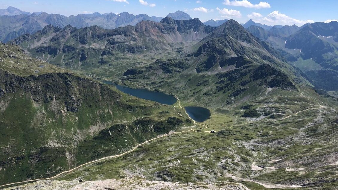 Eine atemberaubende Berglandschaft mit grünen Wiesen und einem klaren See. Im Hintergrund sind hohe Gipfel und ein blauer Himmel zu sehen. | © Martin Huber