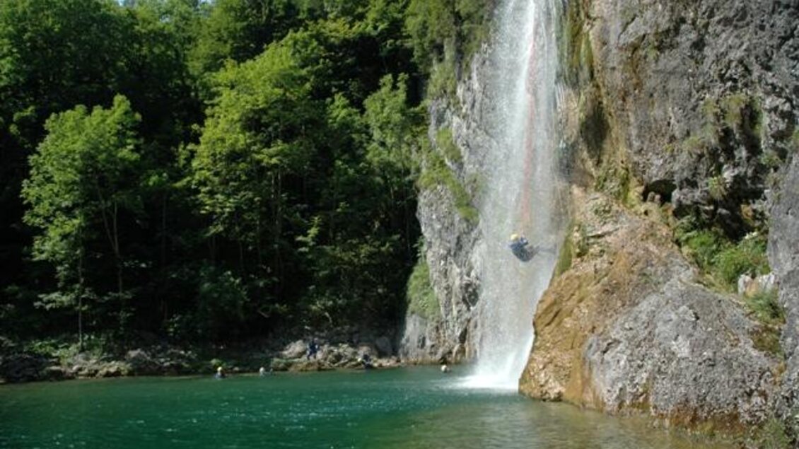 Ein malerischer Wasserfall, der in einen klaren, grün-blauen See stürzt. Umgeben von üppigem, grünem Wald. | © BAC