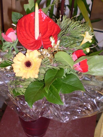 A colorful bouquet with red and yellow flowers and green leaves. The bouquet is wrapped in transparent paper and appears fresh and lively. | © Blumen Sissy