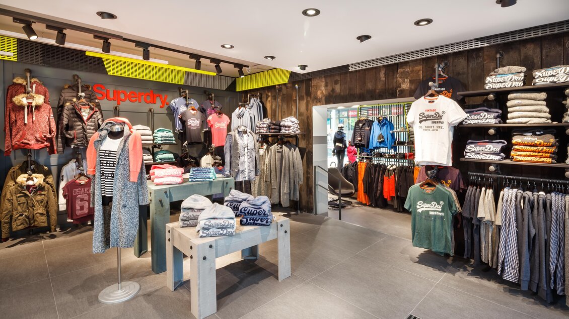 Ein moderner Bekleidungsladen mit verschiedenen Kleidungstücken auf Kleiderständern. Die Wände sind stilvoll gestaltet und die Regale sind mit T-Shirts und Jacken gefüllt. | © Bründl Sports / Christian Wöckinger