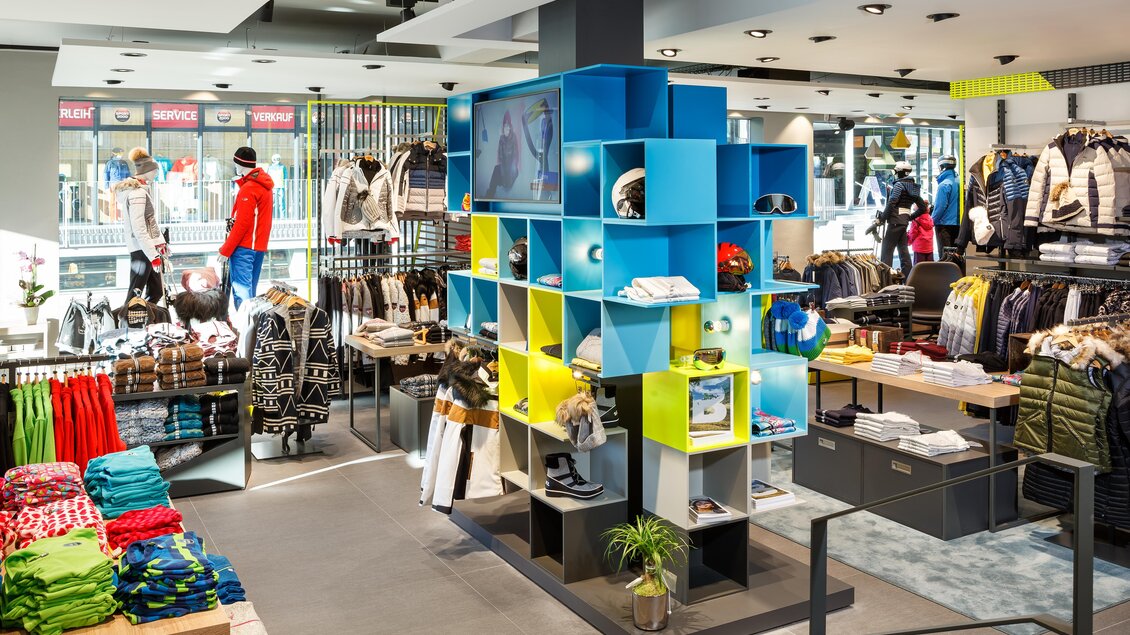 Ein modern eingerichteter Bekleidungsladen mit bunten Regalen und verschiedenen Sportbekleidungen. Im Hintergrund sind Kunden und Kleidung sichtbar. | © Bründl Sports / Christian Wöckinger