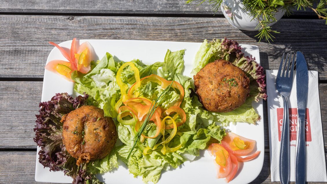 Ein Teller mit zwei goldbraunen Frikadellen auf einem Bett aus frischem Salat. Dekoriert mit verschiedenen Gemüsesorten wie Paprika und Tomaten. | © Netzwerk Kulinarik wildbild