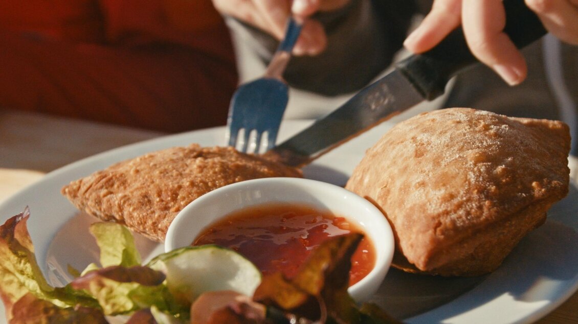 Ein Teller mit zwei knusprigen Teigtaschen und einer Schale mit roter Soße. Dazu liegt ein frischer Salat. | © Gerald Grünwald